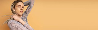 Young nonbinary person touching dreadlocks isolated on yellow with copy space, banner 