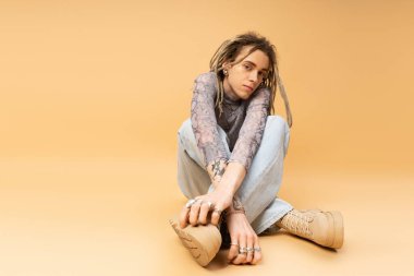 Young tattooed queer person posing on yellow background 