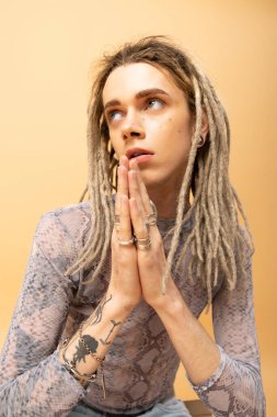 Tattooed queer person doing praying hands gesture on yellow background  clipart