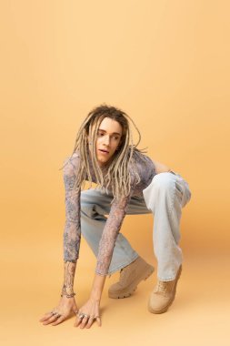 Stylish queer person in jeans and boots posing on yellow background 