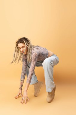 Cheerful queer person with dreadlocks posing on yellow background 