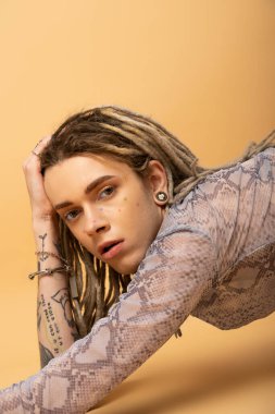 Portrait of tattooed queer person in top with animal print looking at camera on yellow background 