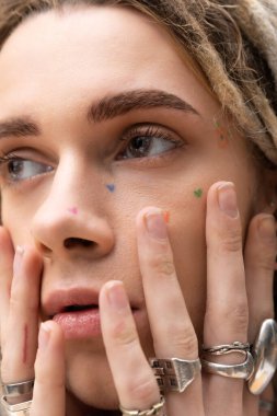 Close up view of young queer person with silver rings on fingers looking away 