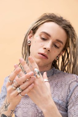 Portrait of nonbinary person touching silver rings on fingers isolated on yellow 