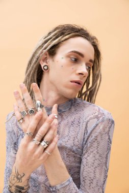 Tattooed queer person in top with animal print touching accessories isolated on yellow 