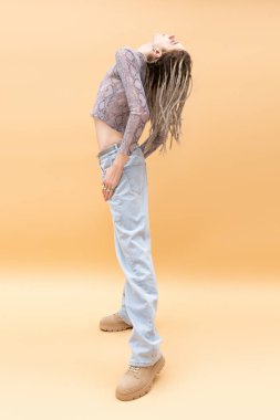 Side view of stylish queer person with dreadlocks posing on yellow background 