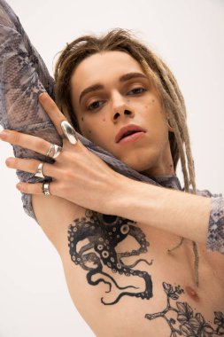 Portrait of tattooed queer person in accessories touching arm isolated on white 