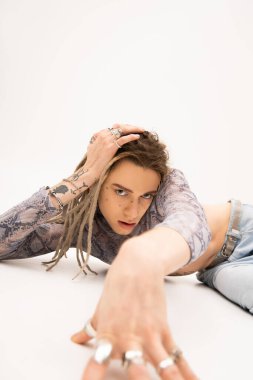 Tattooed nonbinary person looking at camera while lying on white background