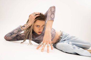 Trendy tattooed queer person posing while lying on white background