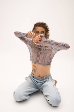 Trendy queer person in crop top looking away while sitting on white background