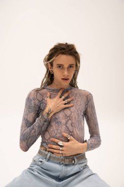 Tattooed queer person with dreadlocks looking at camera isolated on white 