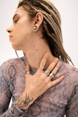 Side view of young tattooed queer person touching neck isolated on white 