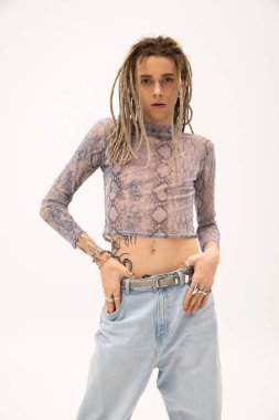 Tattooed nonbinary person in crop top touching jeans isolated on white 