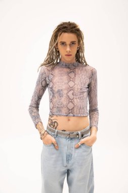 Tattooed queer person in crop top and jeans looking at camera isolated on white 