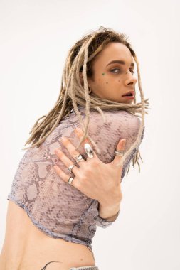 trendy queer model in silver rings and snakeskin print top looking at camera isolated on white