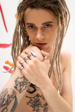 stylish queer person with tattoo and silver finger rings looking at camera on white 