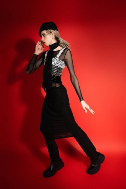 full length of queer person in black and elegant attire on red background with shadow