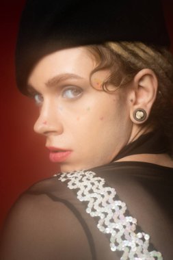 portrait of young and elegant queer person in black beret looking at camera on red background