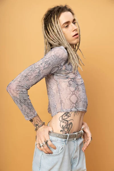 Young queer person with dreadlocks posing isolated on yellow 