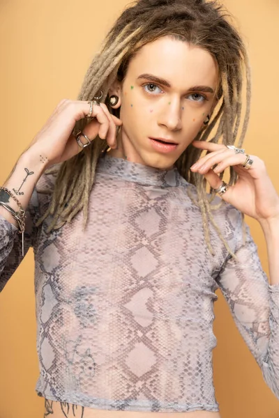 Portrait of tattooed queer person with dreadlocks looking at camera isolated on yellow 