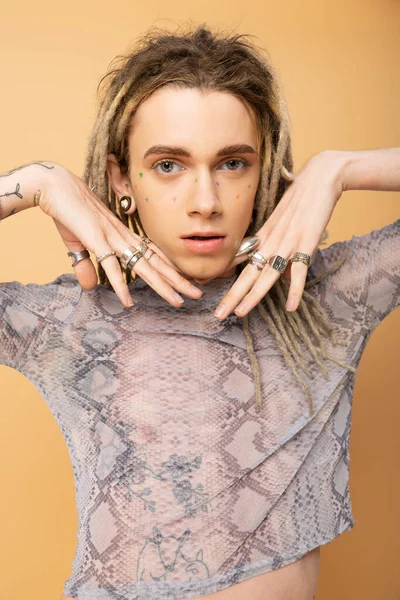 Portrait of tattooed queer person with rings on fingers looking at camera isolated on yellow 