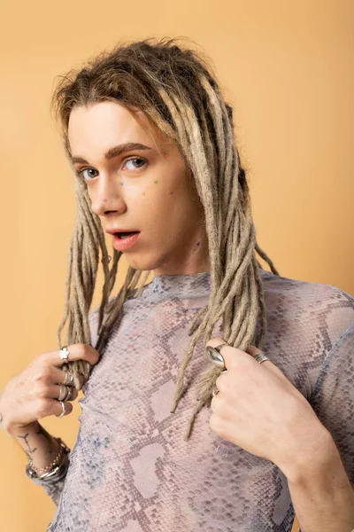 Nonbinary person touching dreadlocks and looking at camera isolated on yellow 