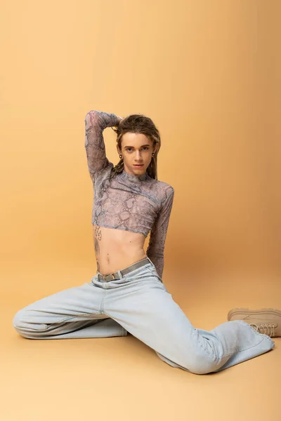 Trendy nonbinary person in crop top posing while sitting on yellow background