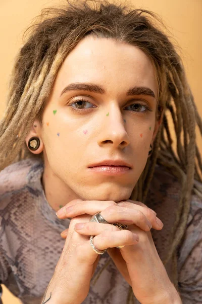 Portrait of young queer person with tattoo on face isolated on yellow