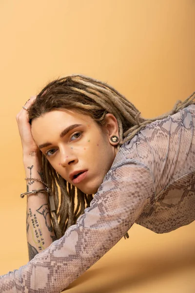 Portrait of tattooed queer person in top with animal print looking at camera on yellow background 
