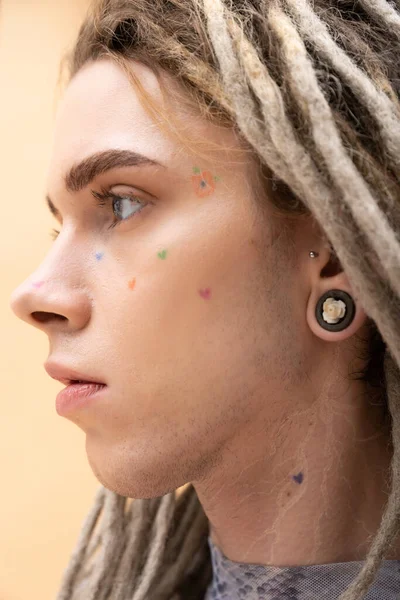 Portrait of young queer person with tattoo on face looking away isolated on yellow
