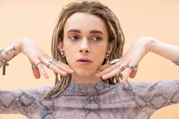 Young tattooed queer person with silver accessories posing isolated on yellow 
