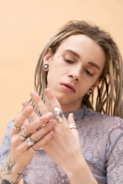 Portrait of nonbinary person touching silver rings on fingers isolated on yellow 