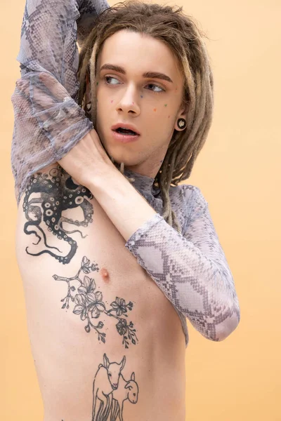 Tattooed queer person in crop top touching arm isolated on yellow 