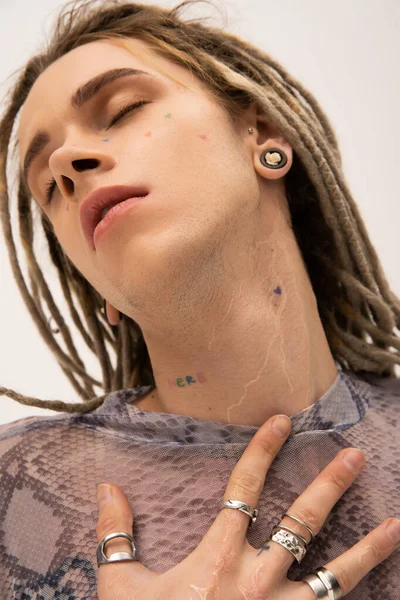 Portrait of young tattooed nonbinary person posing with closed eyes isolated on white 