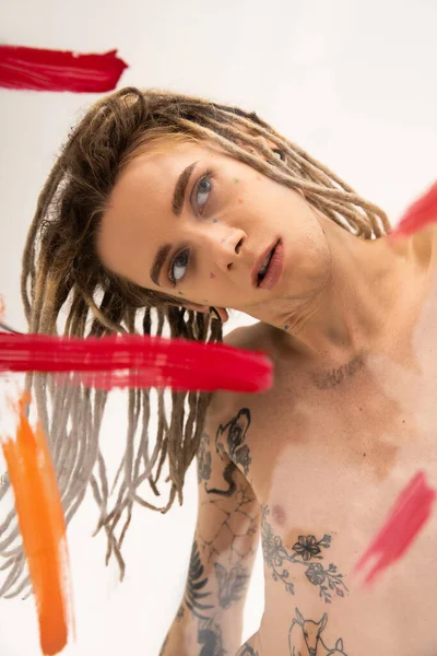 stock image shirtless nonbinary person with dreadlocks posing near red and orange paint strokes on white background