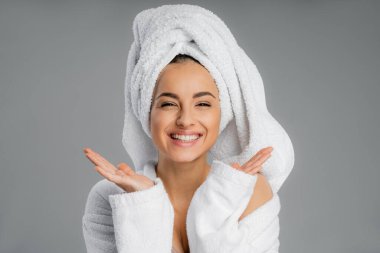 Positive young woman with towel on head looking at camera isolated on grey 