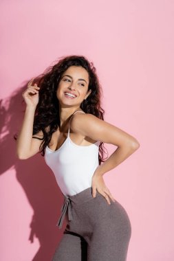 Cheerful young woman in top and pants posing on pink background 