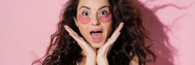 Excited brunette woman with hydrogel eye patches on face on pink background, banner  
