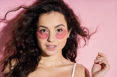Young woman with eye patches on face standing on pink background with shadow 