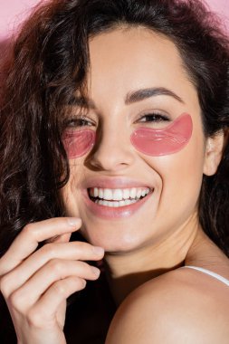 Portrait of curly young woman with eye patches looking at camera on pink background 