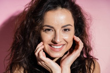 Cheerful freckled woman touching face on pink background  clipart