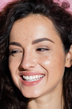 Portrait of smiling woman with freckles looking away isolated on pink 