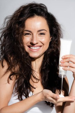 Positive freckled woman pouring lotion on hand isolated on grey 