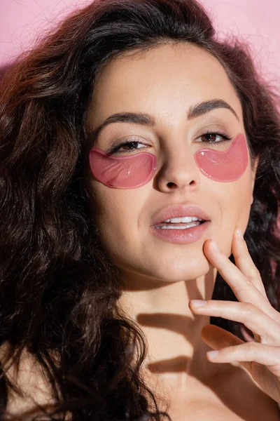 stock image Portrait of curly woman with hydrogel eye patches looking at camera on pink background 