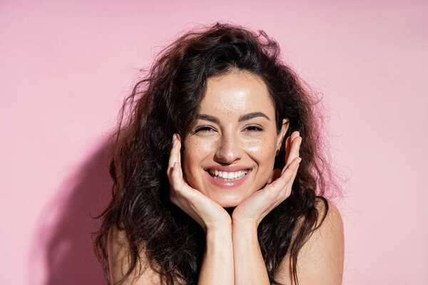 Happy freckled woman looking at camera on pink background 