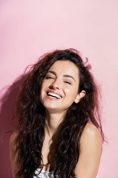 Positive young woman with curly hair looking at camera on pink background 