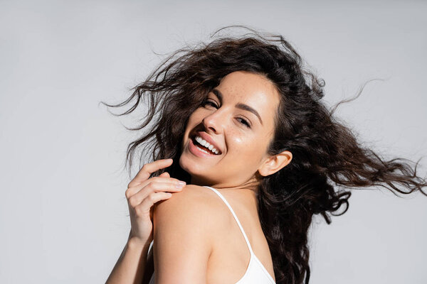 Portrait of freckled woman with curly hair looking at camera isolated on grey 