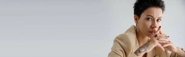 stock image portrait of serious brunette woman with clenched hands looking at camera isolated on grey, banner