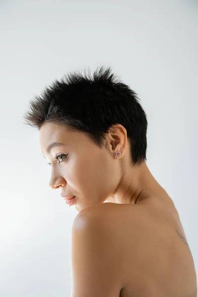 profile of brunette woman with short hair and bare shoulder looking away isolated on grey