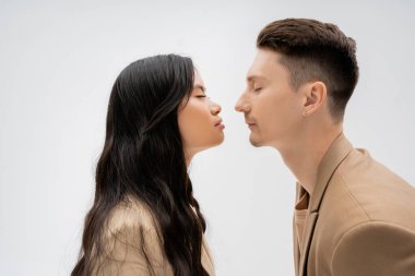 side view of stylish interracial couple standing face to face with closed eyes isolated on grey